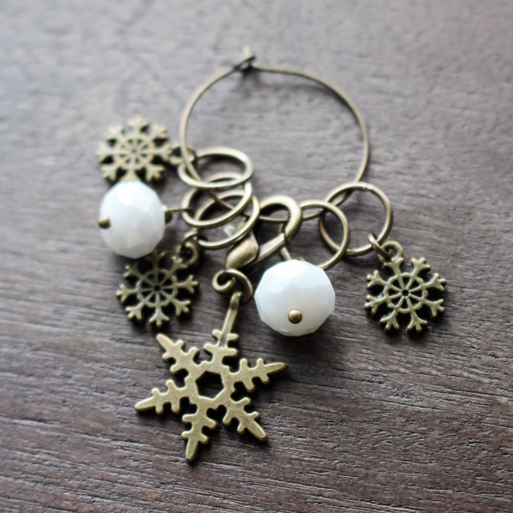 Stitch markers with snowflake and round bead charms on a wooden surface