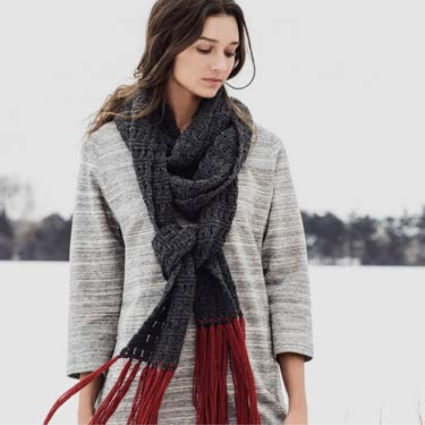 Woman wearing a large knitted scarf with red fringe in a snowy landscape