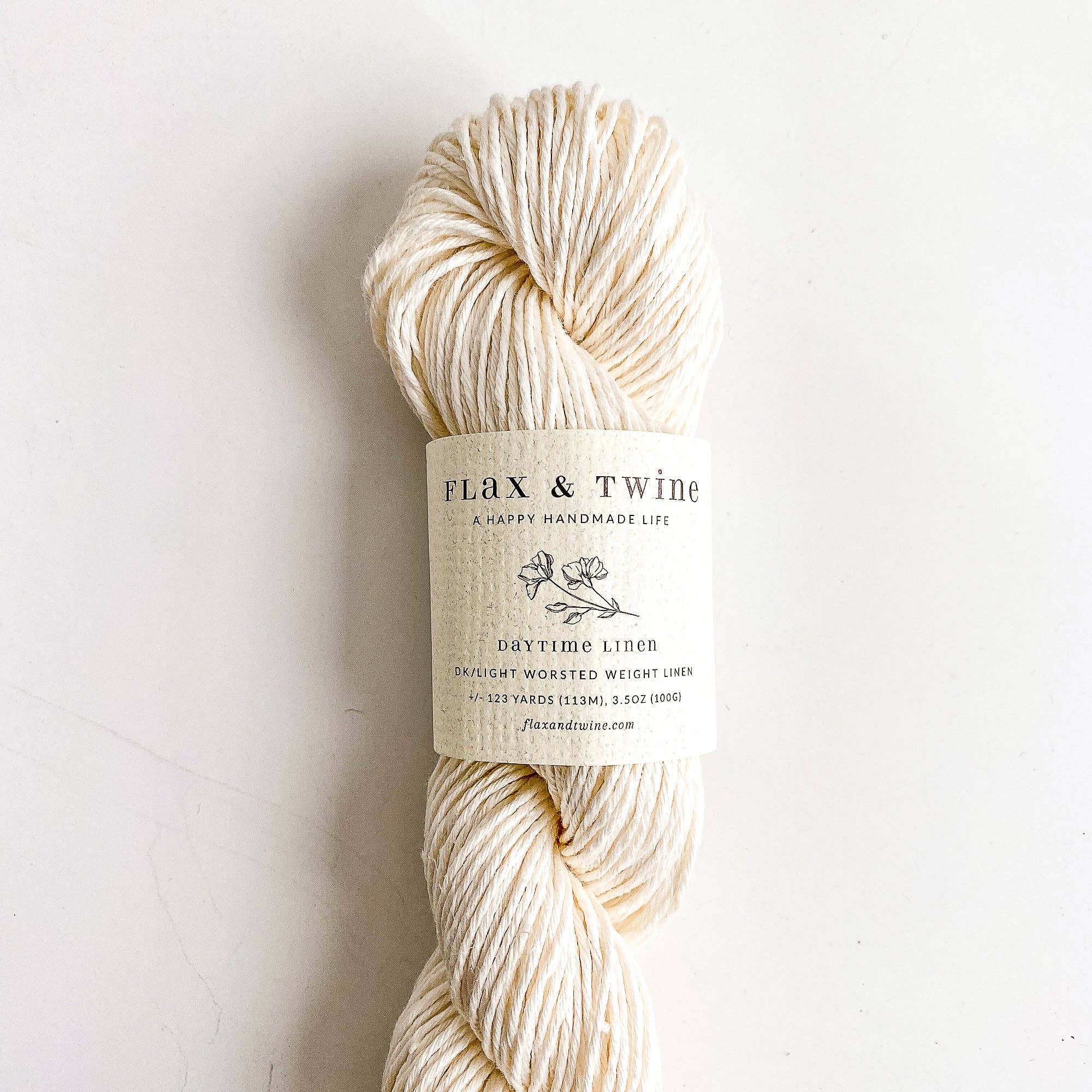 Ball of Flax & Twine Daytime Linen yarn in white with a label on a light background