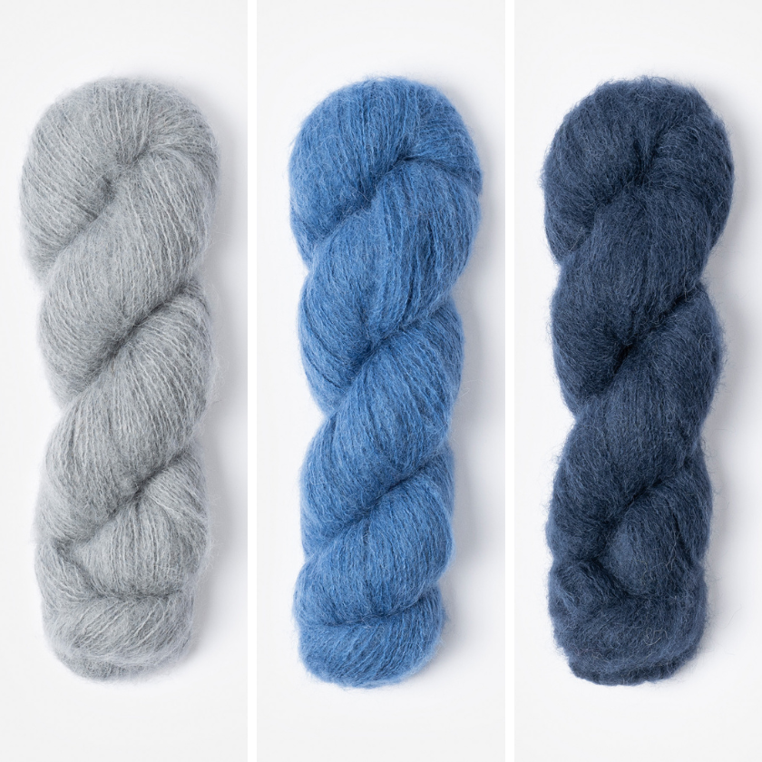 Three skeins of yarn in for the Amsterdam Wrap in grey, blue, and dark blue on a white background