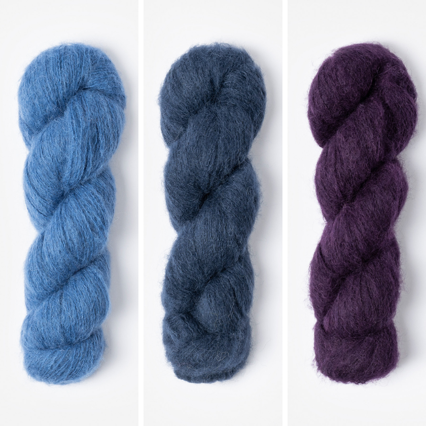 Three skeins of yarn in for the Amsterdam Wrap in blue, dark blue, and purple on a white background