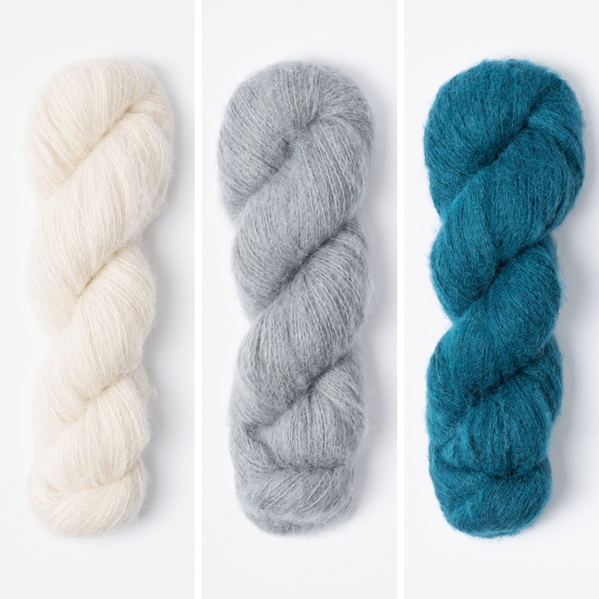 Three skeins of yarn in for the Amsterdam Wrap in white, grey, and aqua blue on a white background