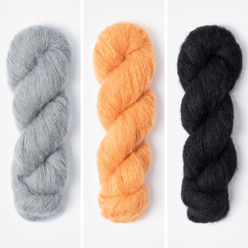 Three skeins of yarn in for the Amsterdam Wrap in grey, orange, and black on a white background