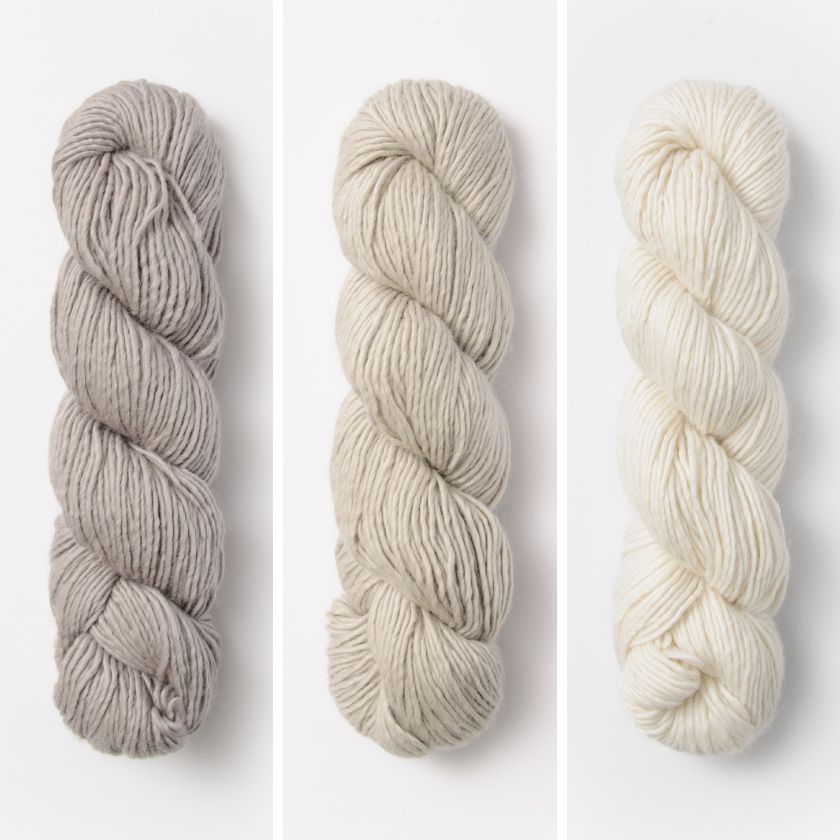Three skeins of yarn for the Bianca Wrap in beige, cream, and white on a white background