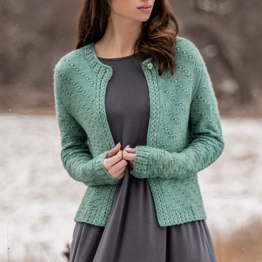 A woman wearing a green Ocean Bloom Cardigan over a gray dress, standing outdoors with a trees in the background.