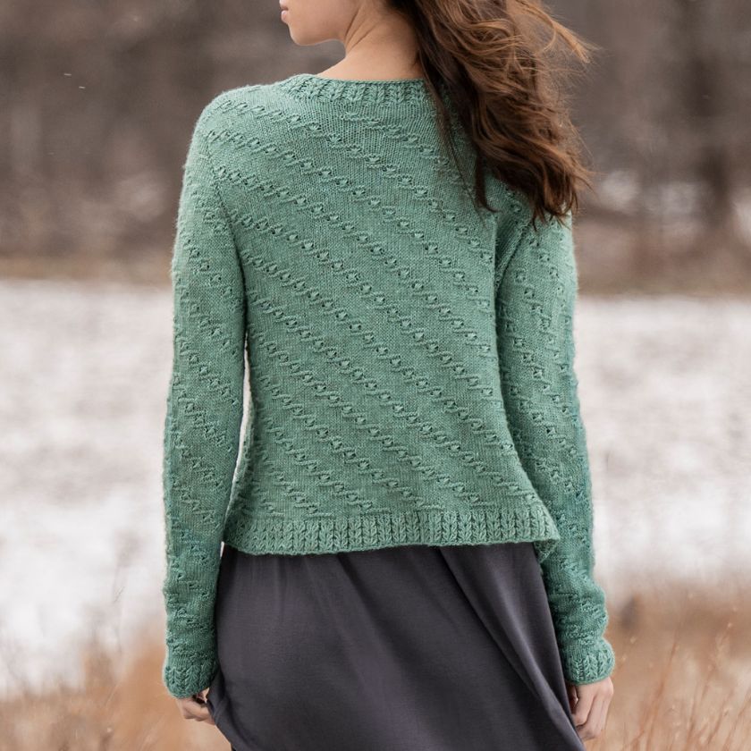 Model showcasing the back of the Ocean Bloom Cardigan over a gray dress, standing outdoors with a trees in the background.