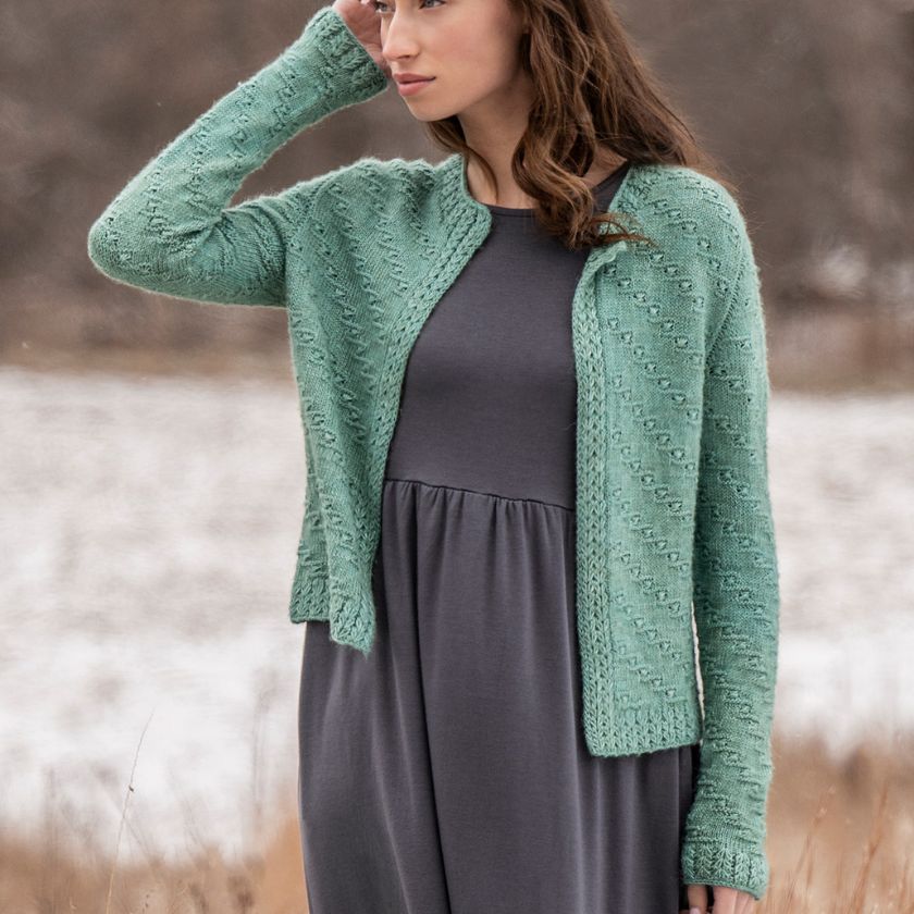 A model wears the green Ocean Bloom Cardigan over a gray dress, standing outdoors with a trees and snow
