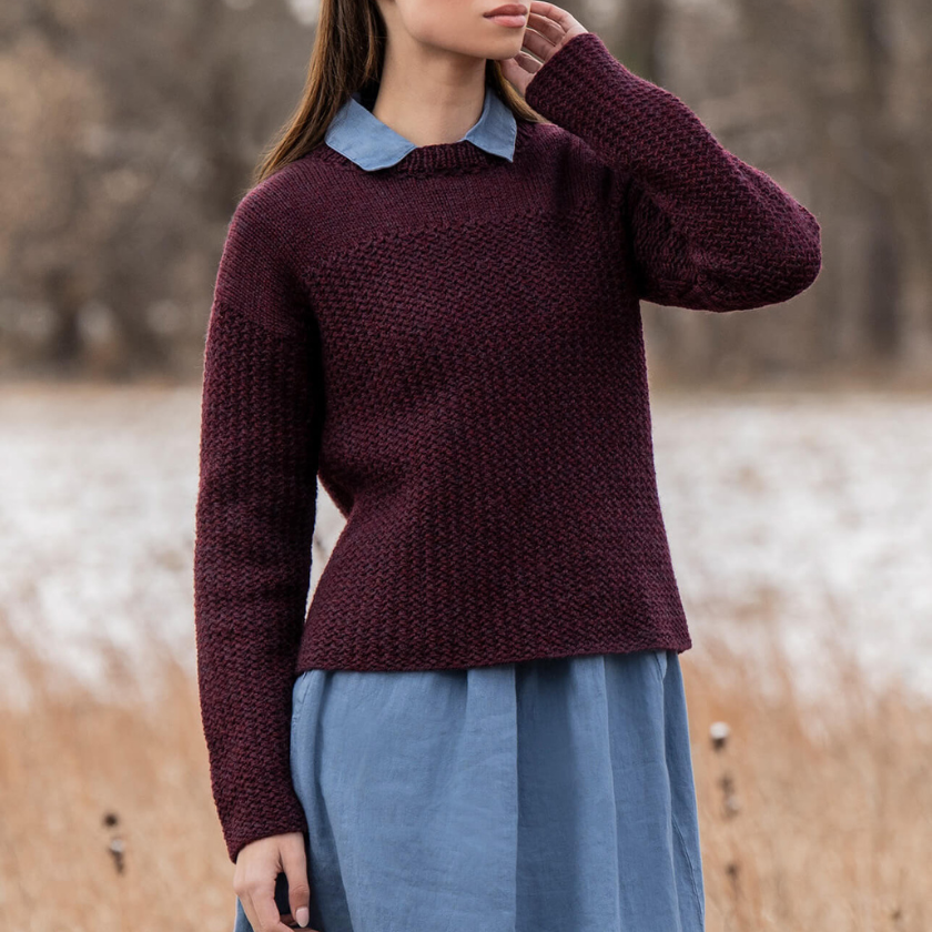 Person wearing a maroon Park Avenue pullover over a blue shirt with a blurred natural background