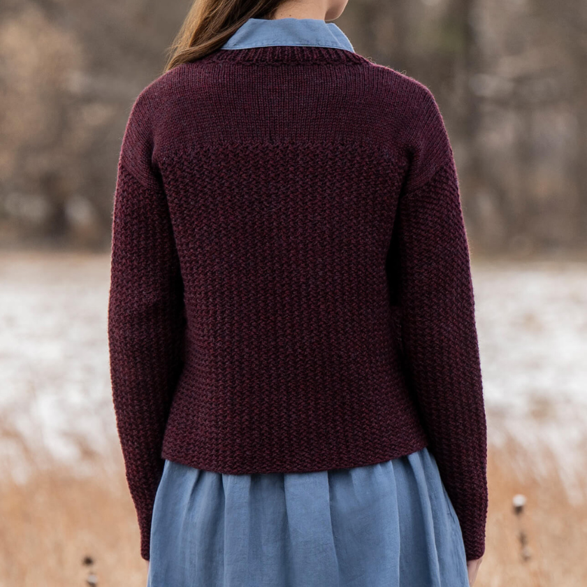 Person wearing a maroon knitted Park Avenue pullover over a blue shirt in a snowy landscape