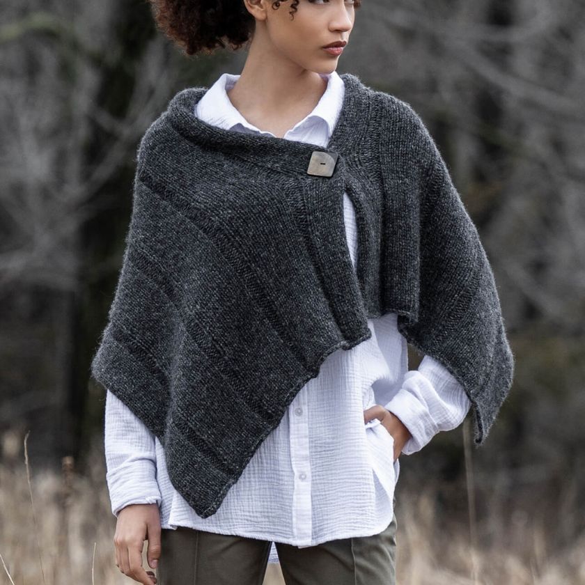 Model wearing a dark gray Sasha Wrap over a white garment against a blurred natural background