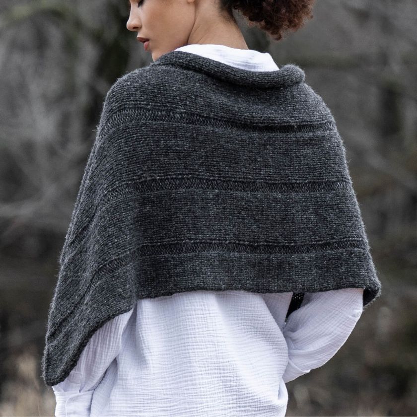 Model wearing a dark gray Sasha Wrap over a white garment against a blurred natural background