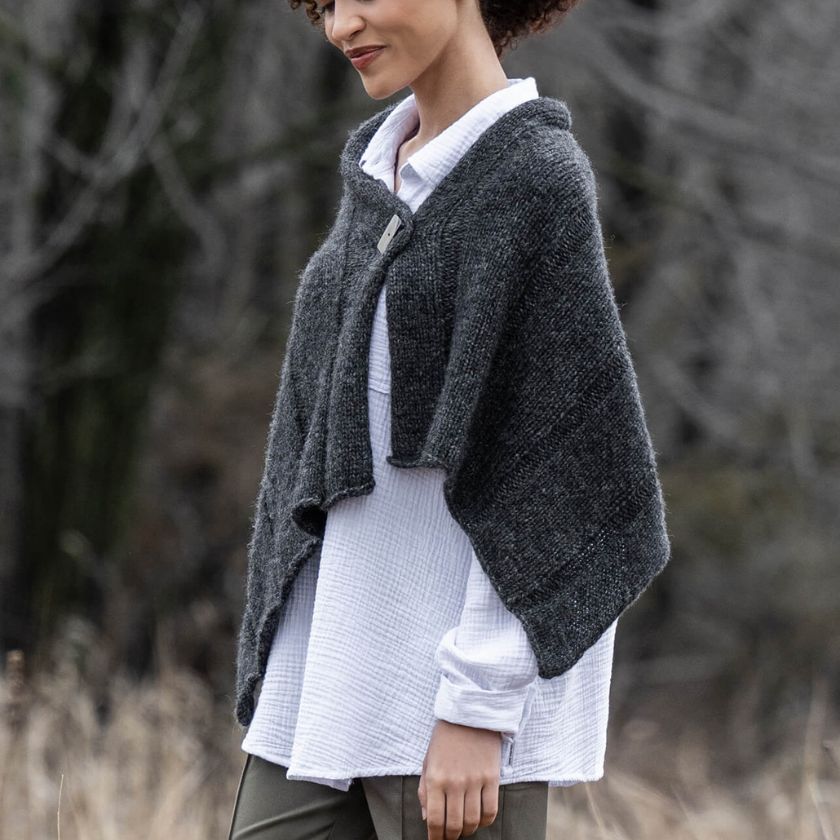 Model wearing a dark gray Sasha Wrap over a white garment against a blurred natural background