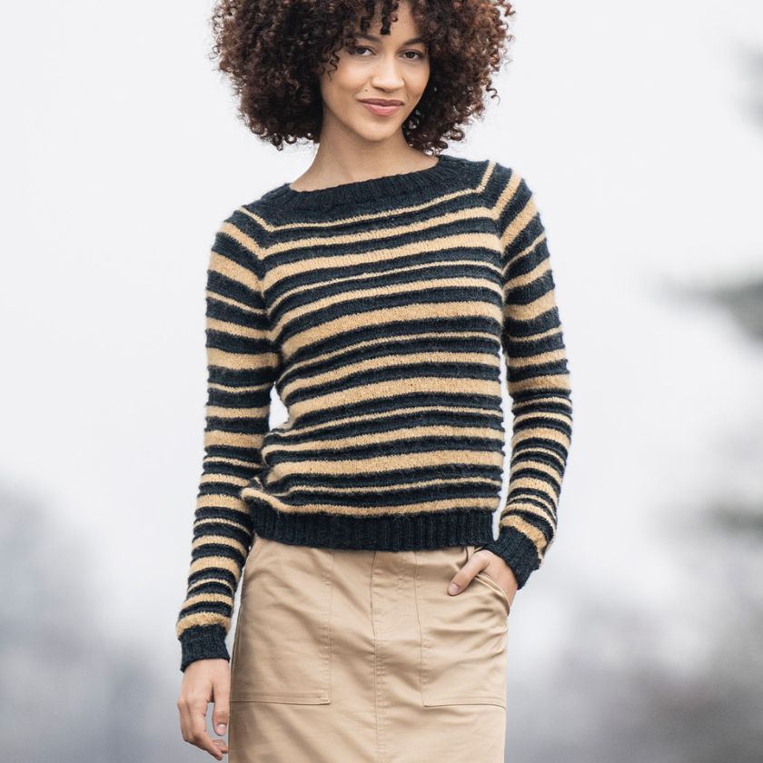 A model smiles while wearing a Saturnalia Pullover with varying widths of dark and light horizontal stripes.