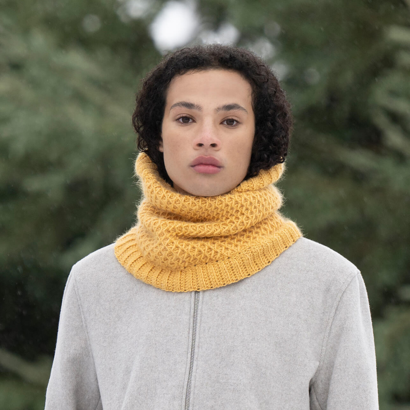 Model wearing the Serene Sunset Cowl knit in Blue Sky Fibers Suri Merino in Golden Hour, showing the textured smock stitch and ribbed edge. The Dizzy Knitter