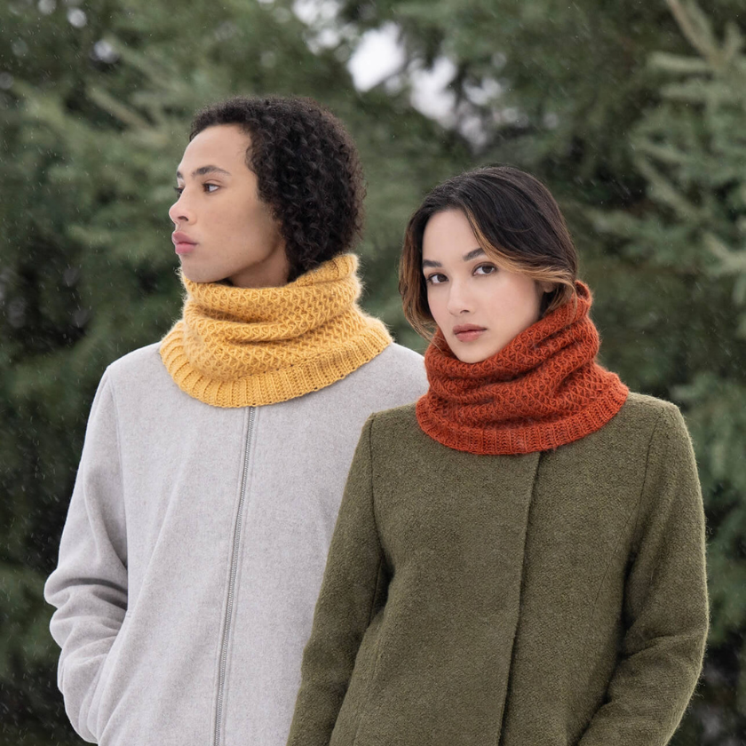 Two models wearing the Serene Sunset Cowl in Golden Hour and Autumn, knit in Blue Sky Fibers Suri Merino with a richly textured smock stitch. The Dizzy Knitter