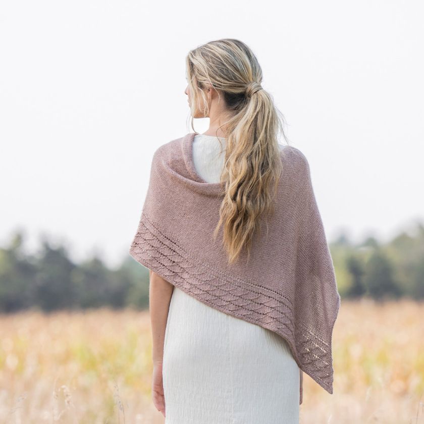 Model shows the back of the Serenity Wrap knitting project over a white dress
