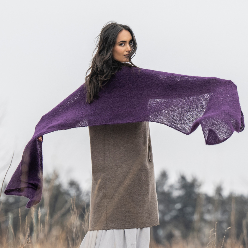A model showing off the full width of the Stardust Wrap knitting kit in Elderberry