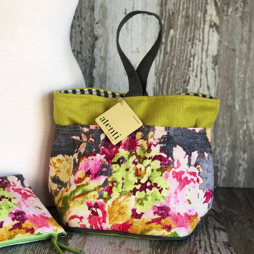 Floral-patterned fabric knitting bag and pouch with an atenti tag on a wooden surface.