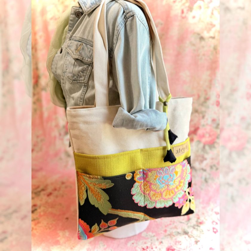 Tote bag with floral design and yellow accent held by a mannequin against a soft pink floral background