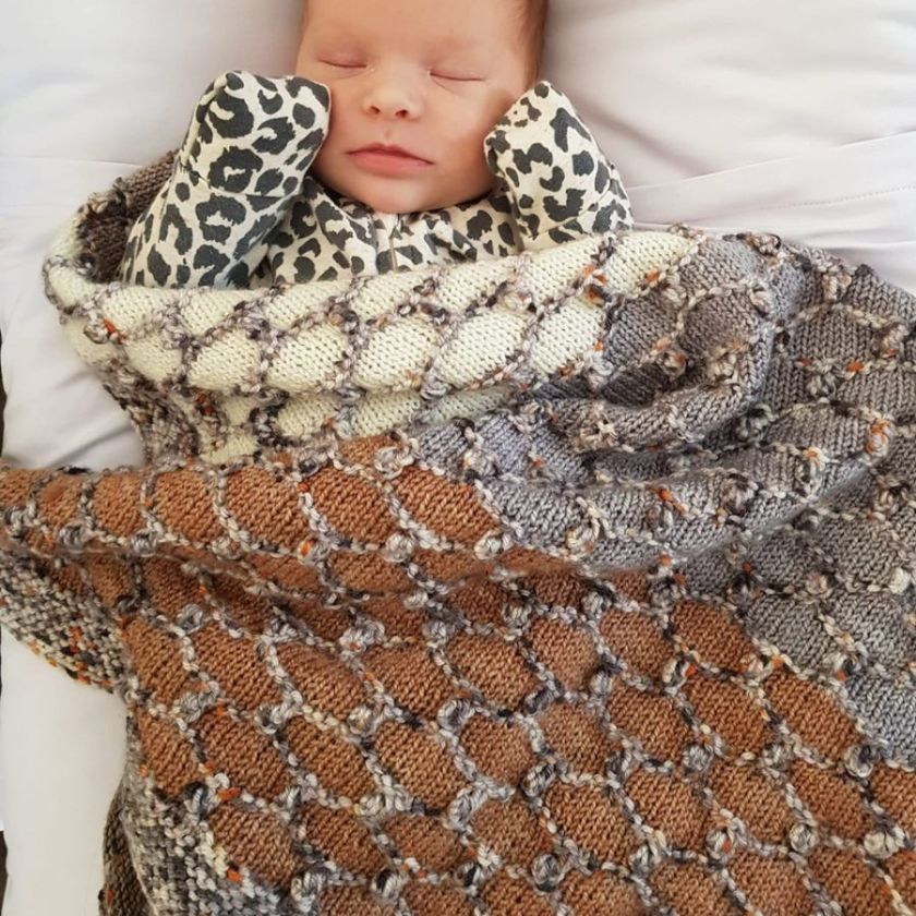 A baby wrapped in the neutral Beehive Baby blanket by cowgirlblues
