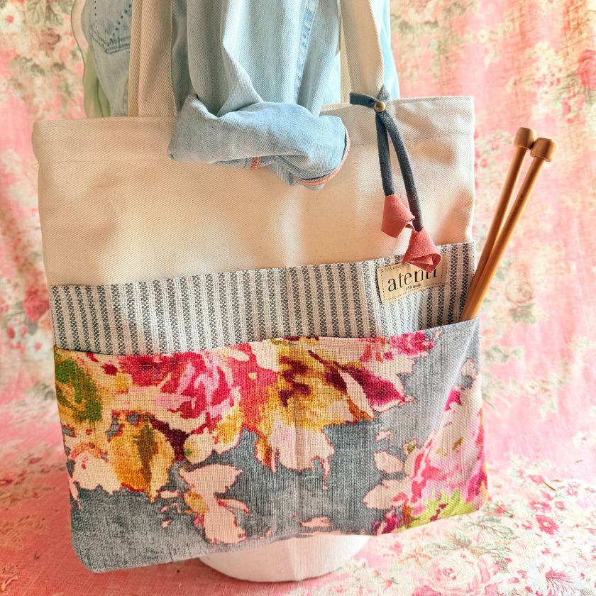 Atenti knitting bag with floral pattern and striped section held by a mannequin on a floral background.