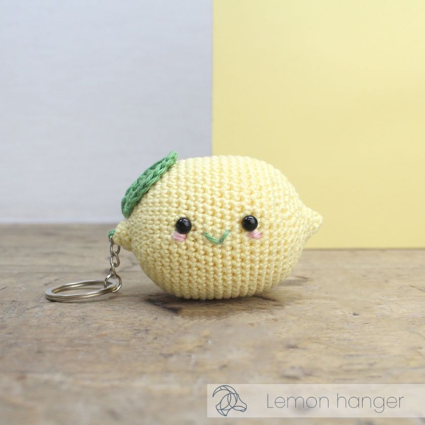 Crocheted lemon-shaped keychain with a happy face on a wooden surface.