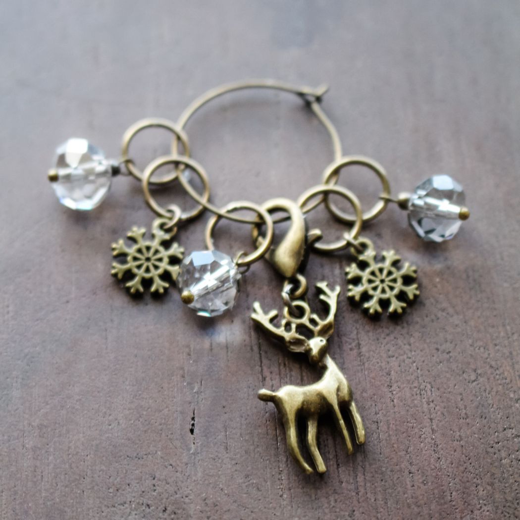 Brass stitch markers with reindeer and snoflake charms on a wooden surface