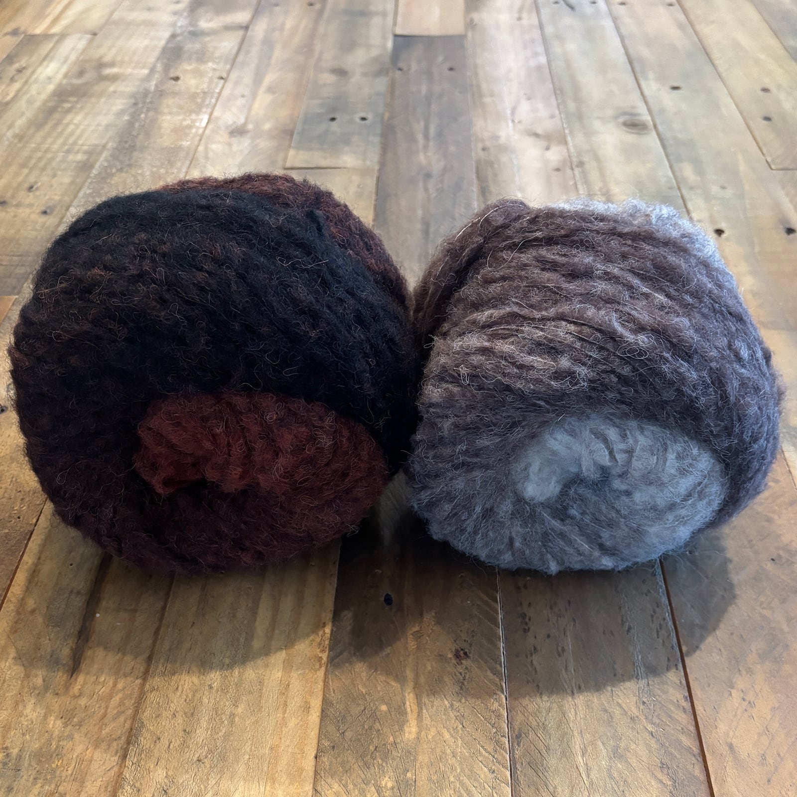 Two skeins of super bulky Piuma Alpaca Degradé yarn in Taupes and Rusts for the Degradé Drift Scarf on a wooden background