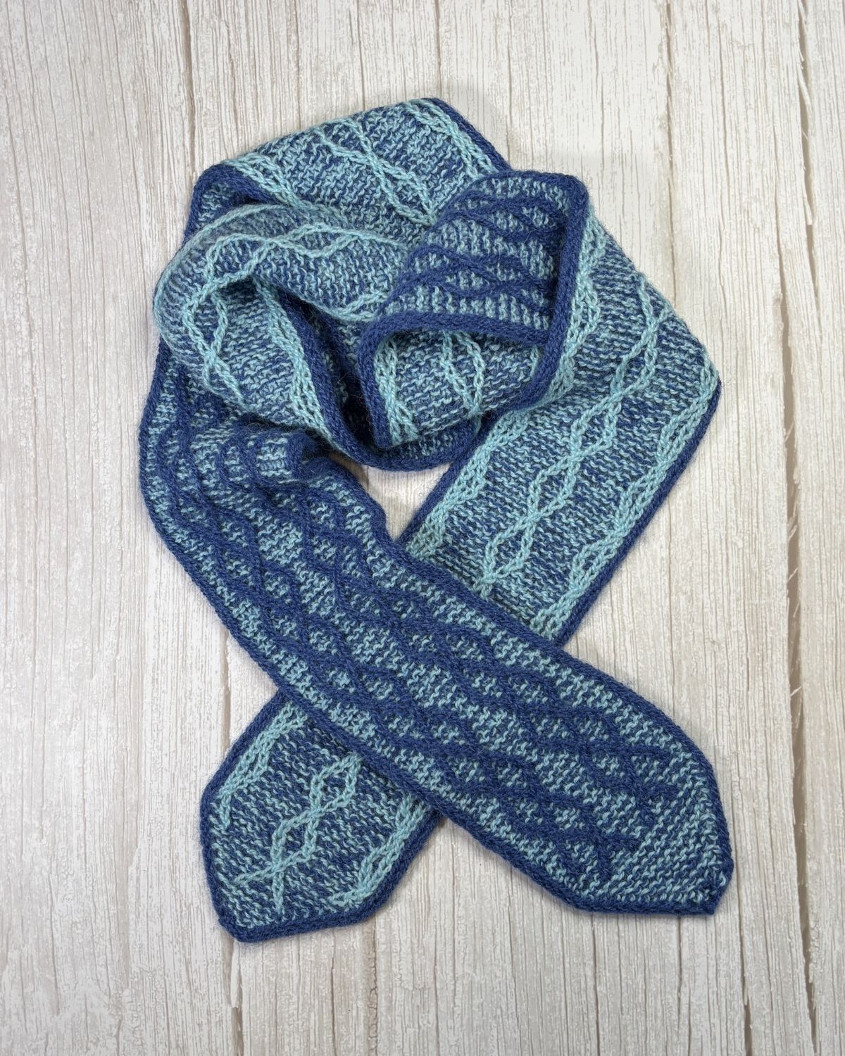 Blue knitted scarf showcasis fission knitting on a light wooden surface