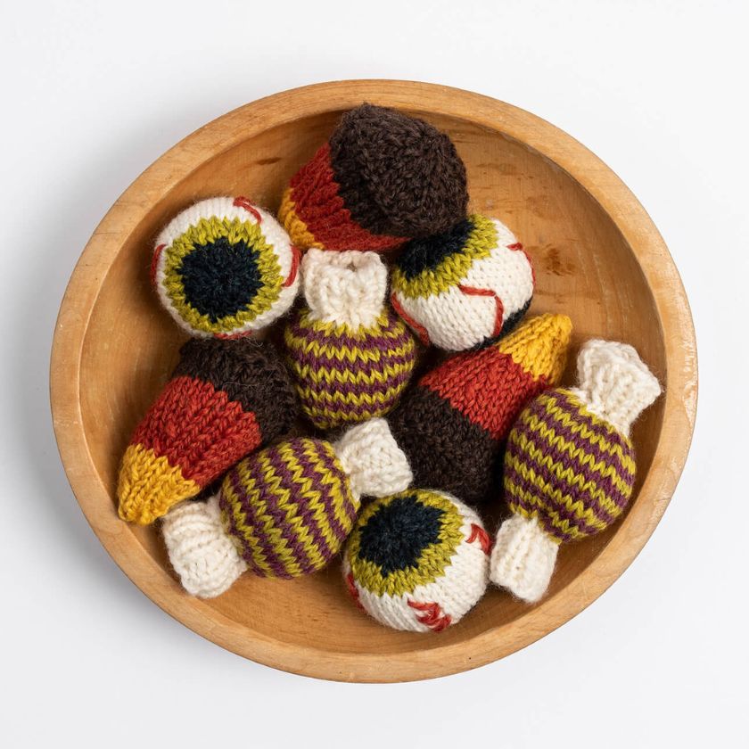 Wooden bowl filled with knitted toys resembling candies and eyeballs on a white background
