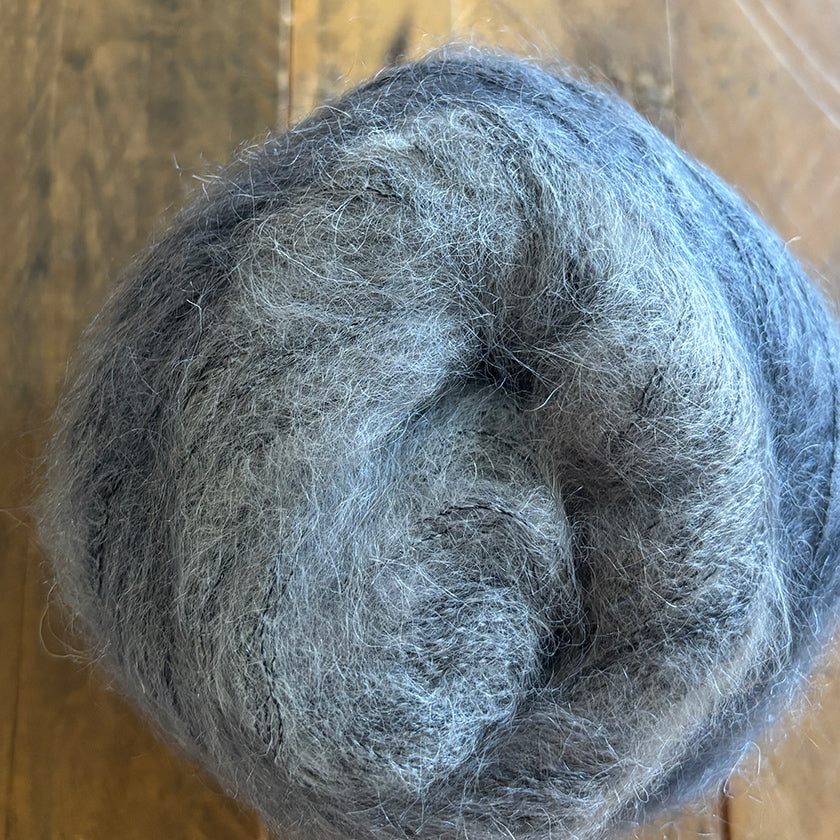 Ball of Poema Mohair yarn in multiple greys on a wooden surface