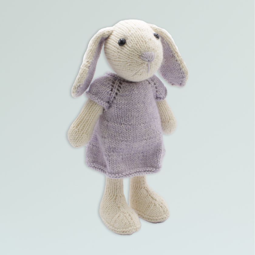 Knitted Amigurumi toy bunny in a purple dress on a light gray background