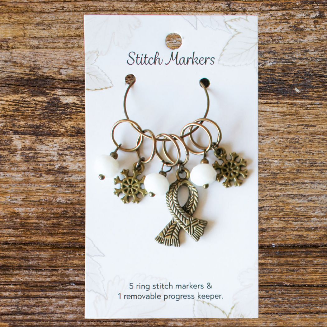 Set of winter themed stitch markers on a white card with text on a wooden surface