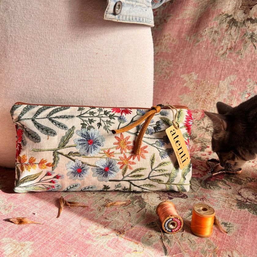 The Wildflower Pouch from Atenti Bags on a floral fabric amongst sewing gear as a cat sniffs a pair of scissors