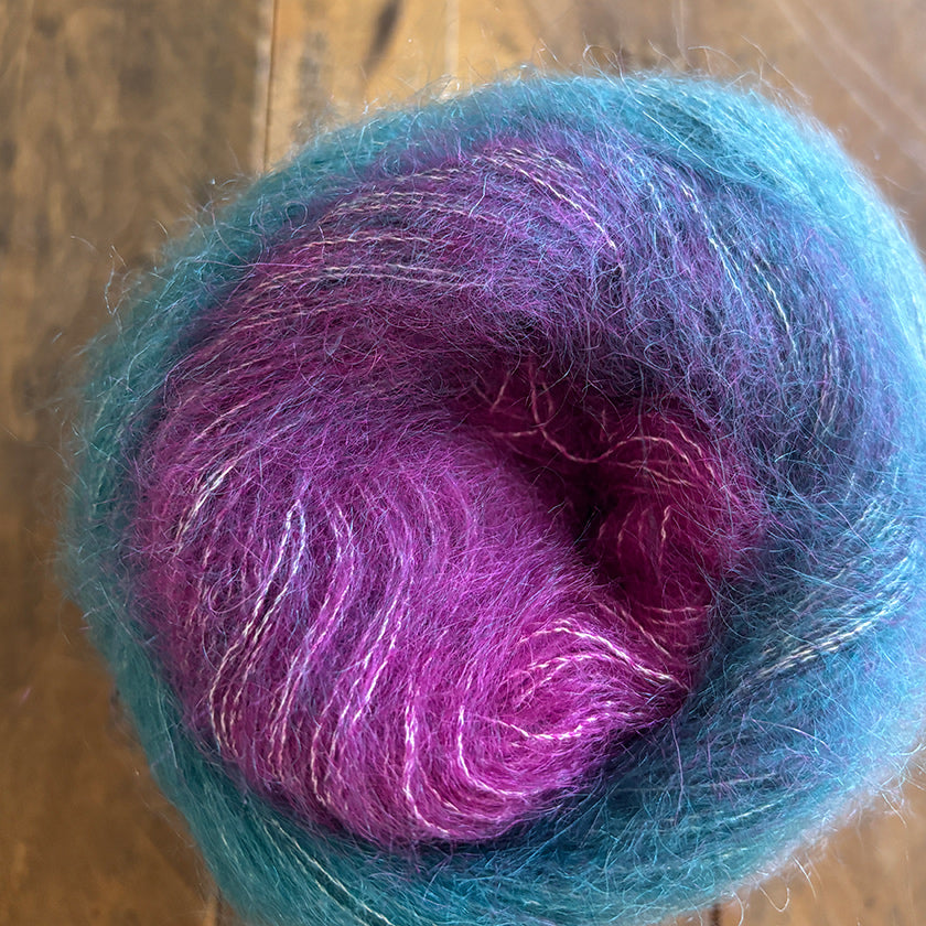 Ball of Poema Mohair yarn in Magenta, Teal, and Denim on a wooden surface