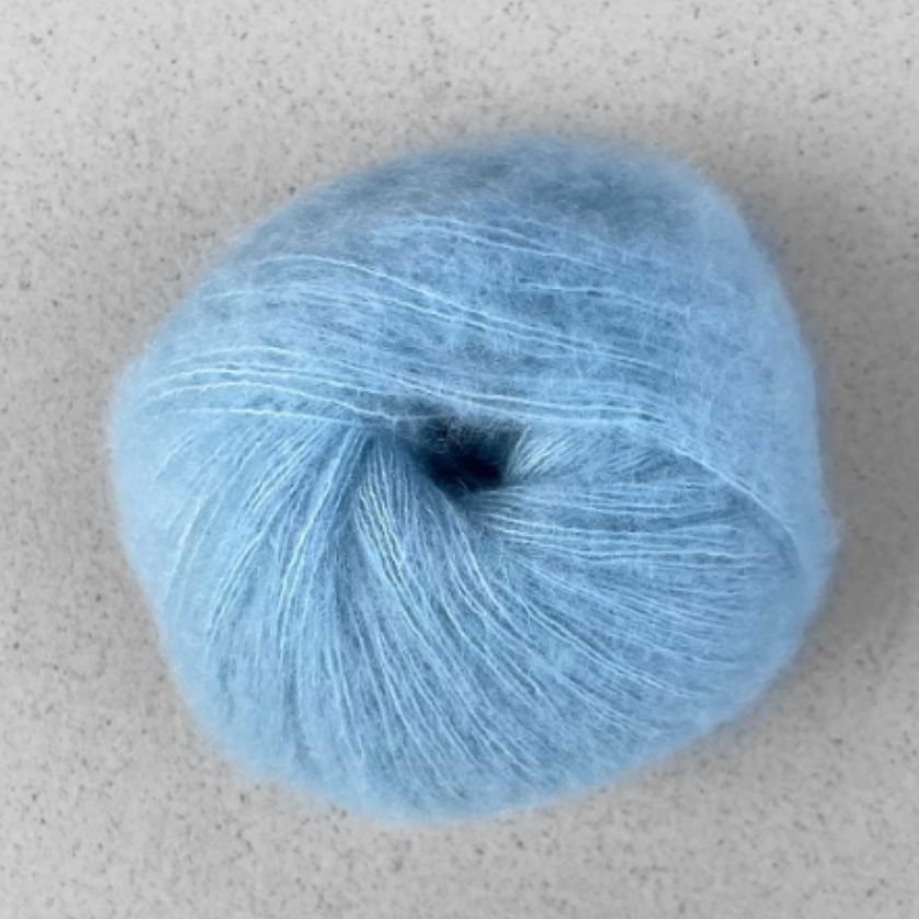 A ball of light blue Manada yarn by Pascuali made from a blend of merino sheep, sumptuous Mongolian yak wool, and silk