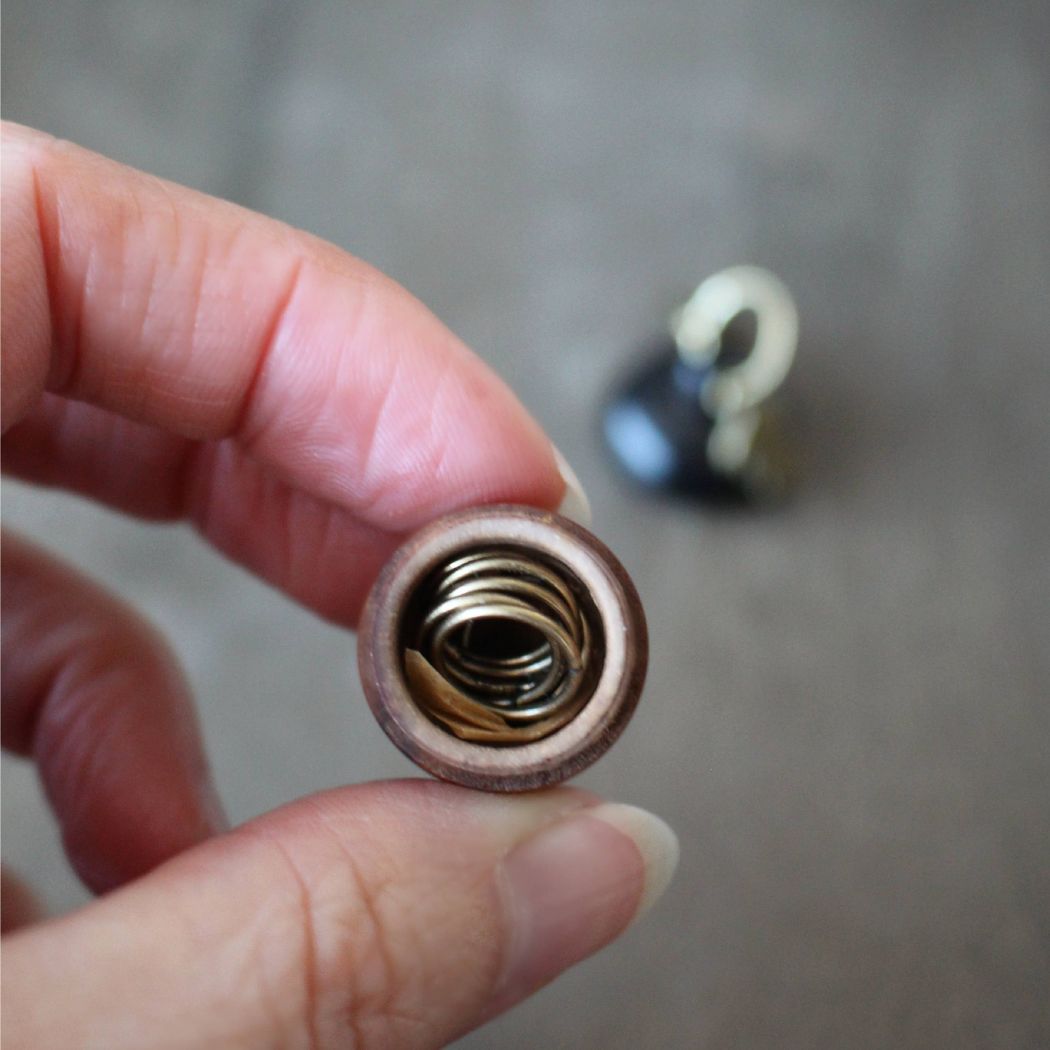 Decorative stitch markers in an acorn holder on a wooden surface.