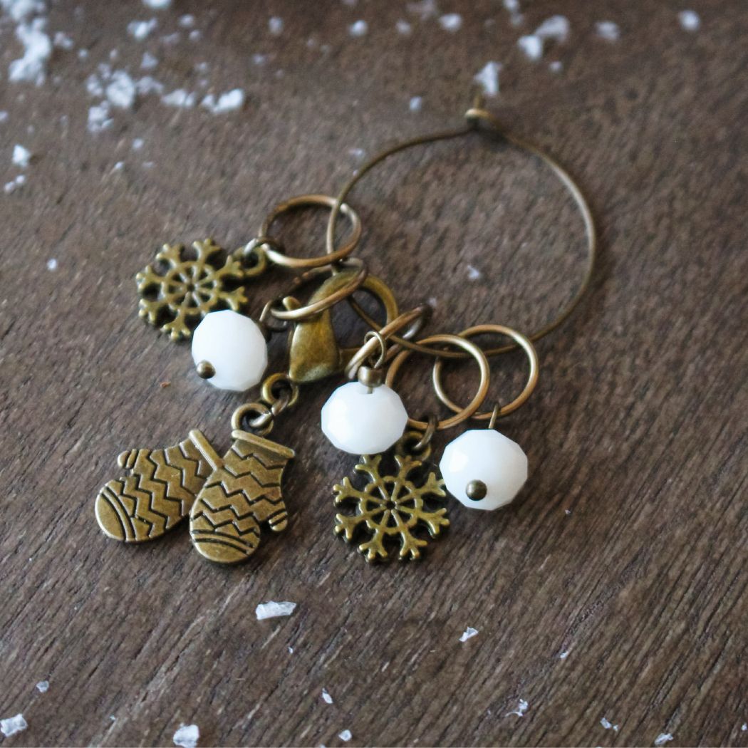 Decorative stitch markers with winter themed charms on a wooden surface.