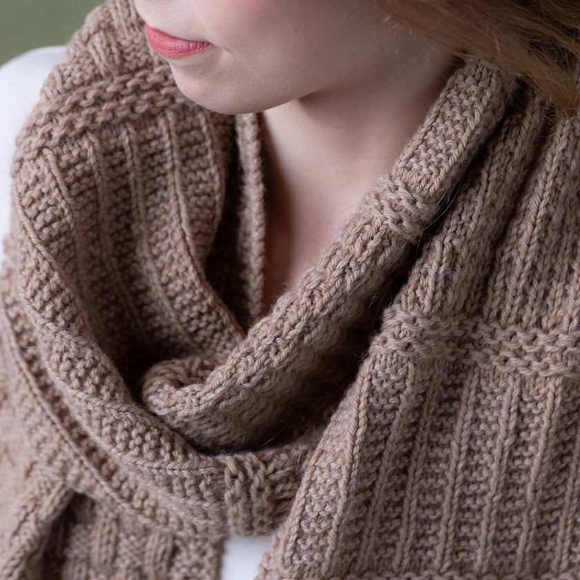 Close-up of a person wearing a brown knitted Pascuali Mix it Up scarf with a neutral background