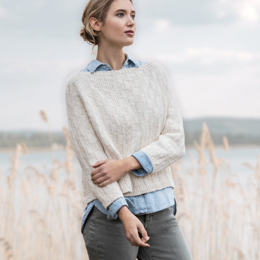 Model wears cream colored sweater knitted from Woolstok worsted organic cotton yarn