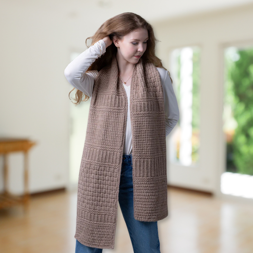 Woman wearing a long brown knitted Pascuali Mix it Up scarf indoors