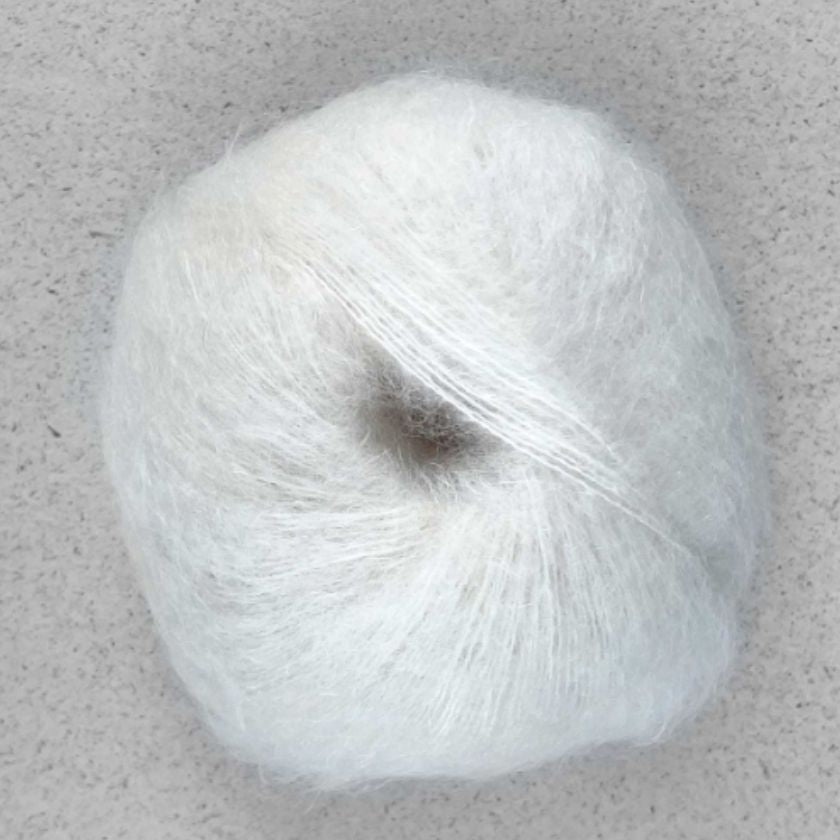 A ball of white Manada yarn by Pascuali made from a blend of merino sheep, sumptuous Mongolian yak wool, and silk