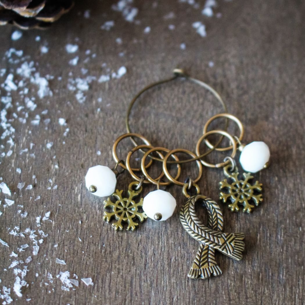 Decorative stitch markers with snowflake, ribbon, and circular charms on a wooden surface.