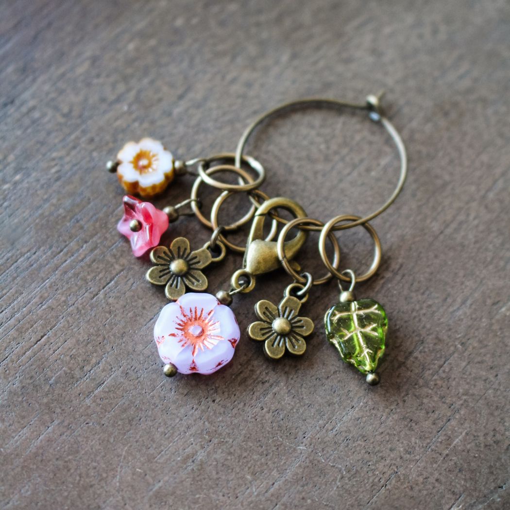 Decorative stitch markers with floral and leaf charms on a wooden surface