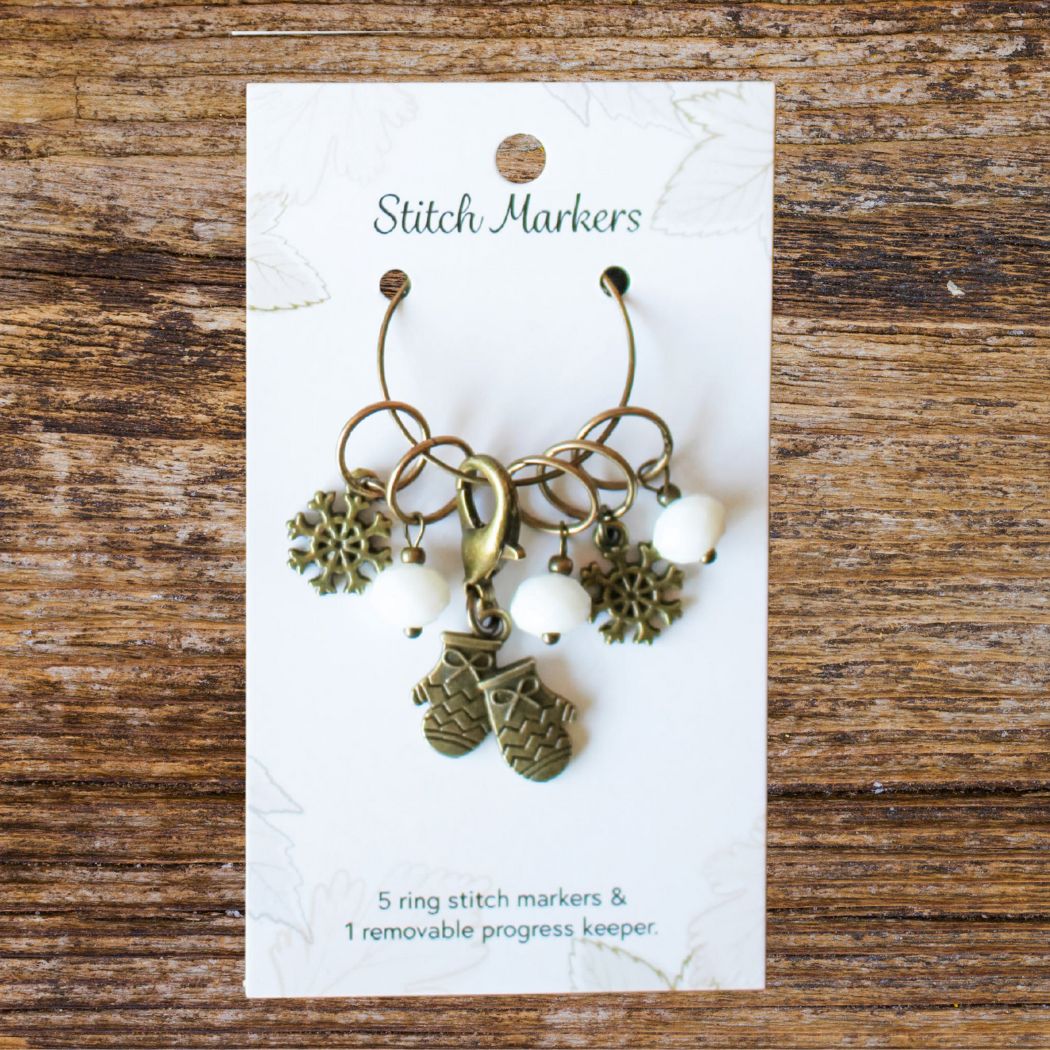 Stitch markers on a card with winter themed charms on a wooden surface