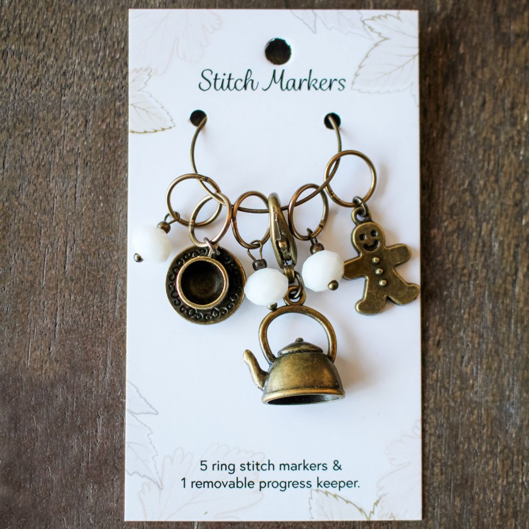 Set of holiday themed stitch markers with decorative charms on a white card with text.