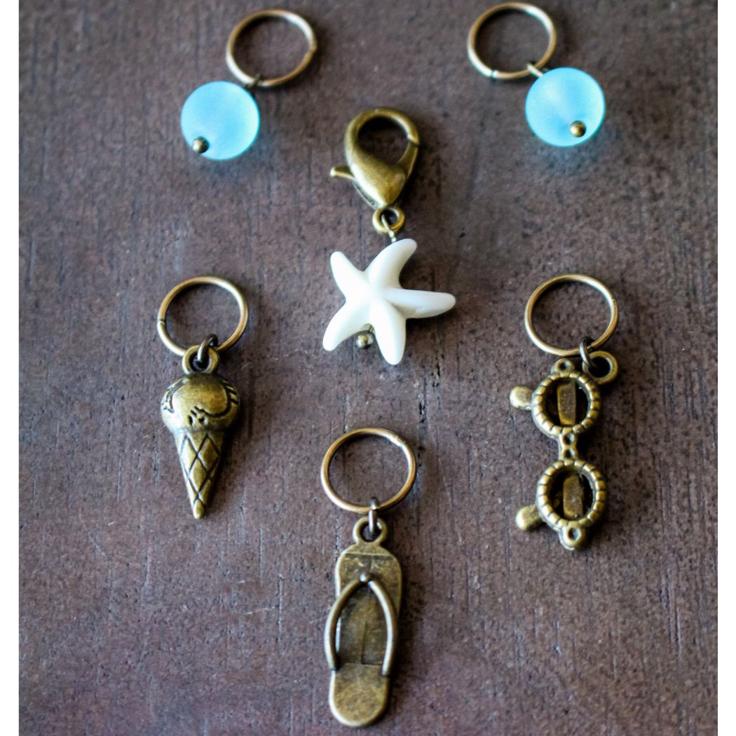 Collection of small bronze summer themed stitch markers on a brown background