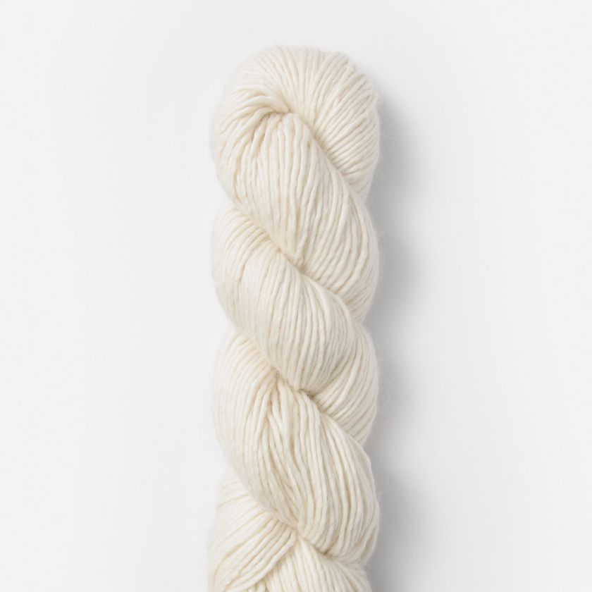 Coiled skein of Suri Merino Ice Cap yarn on a light gray background