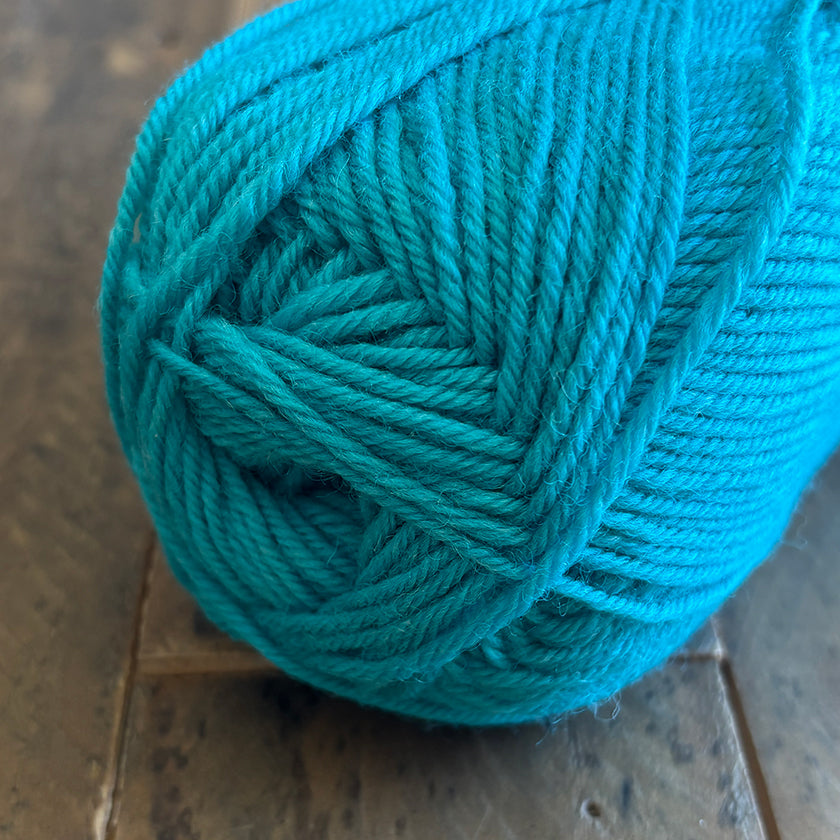 Ball of Ella Rae Classic Wool yarn in Tame Teal on a wooden surface
