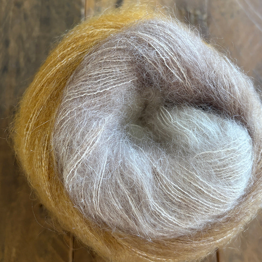 Ball of Poema Mohair yarn in Tan, Camel, and Ecru on a wooden surface